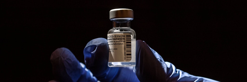 Hand hält Ampulle mit Biontech/Pfizer Impfstoff.