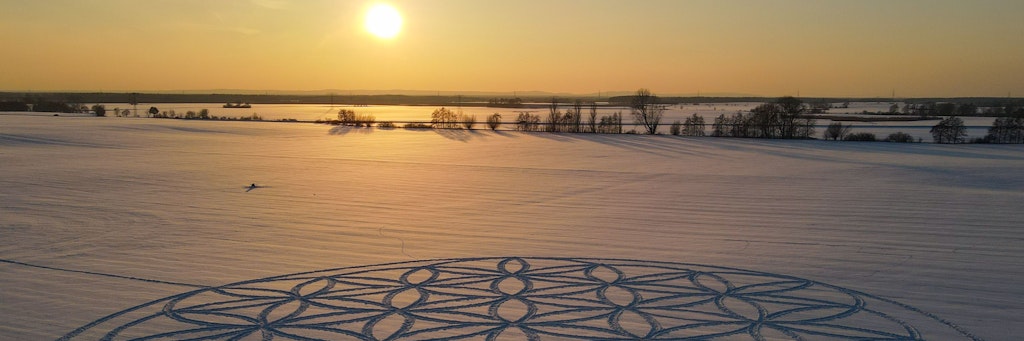 Eine „Blume des Lebens“ hat ein Künstler in den Brandenburger Schnee gefräst, über dem die Sonne scheint.