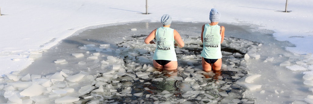 Zwei Frauen steigen in das eisige Wasser eines Sees. 