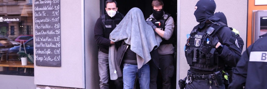 Polizisten führen einen der Verhafteten aus einem Haus.<br><br><br>
