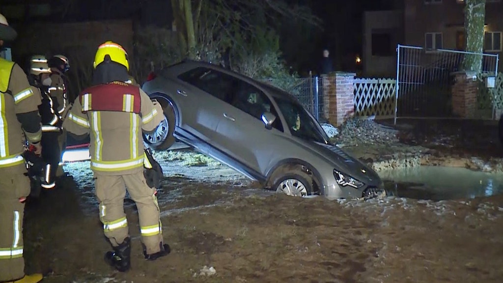 Ein Krater, in dem ein Auto steckt, ist vor einer Grundstückseinfahrt im Stadtteil Hermsdorf zu sehen. Das Fahrzeug war in das Loch gefahren und musste von der Feuerwehr wieder herausgezogen werden. 