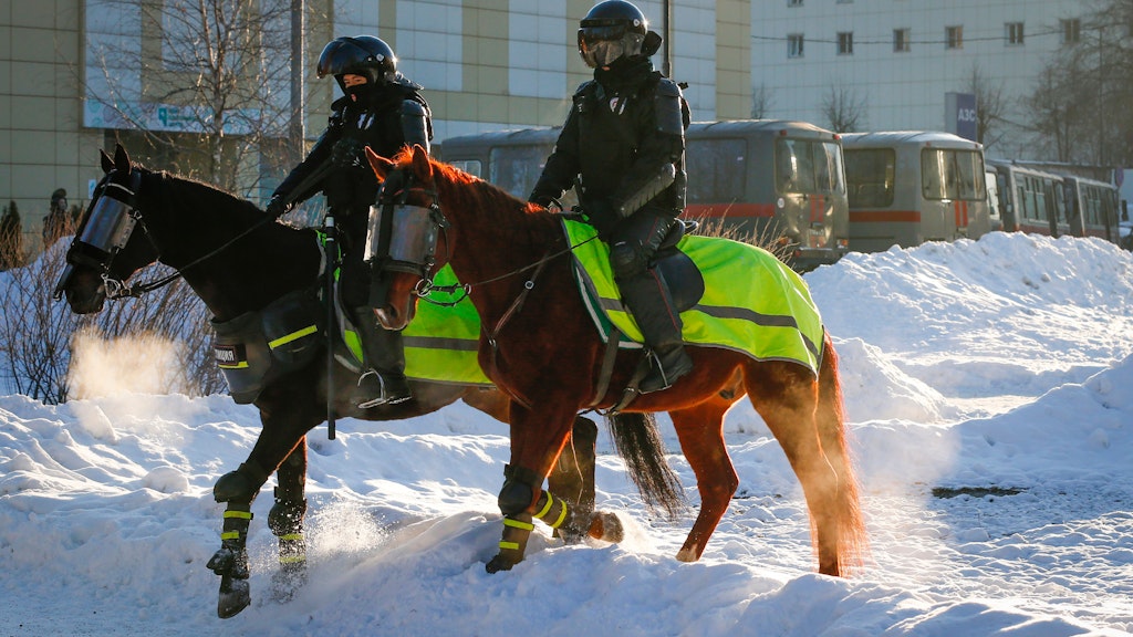 Diverse Mannschaftswagen stehen in der Nähe des Gerichts, davor zwei Polizisten zu Pferde. 