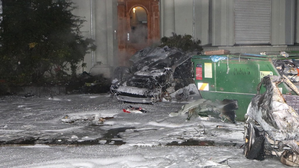  Die ausgebrannten Hälften des Autos liegen neben dem Schuttcontainer, umgeben von Löschschaum.