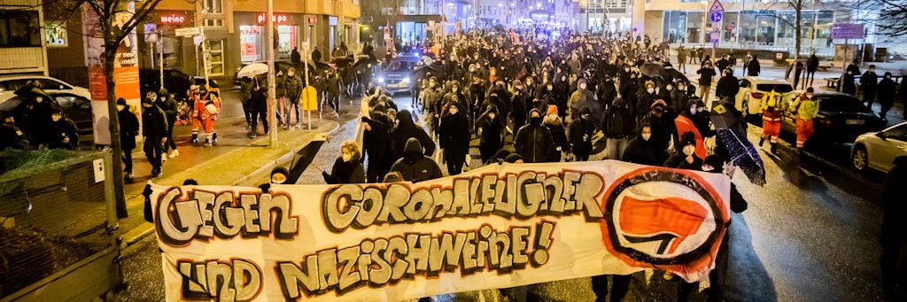 Der Zug einer Demonstration linker Gruppen mit einem Banner mit der Aufschrift "Gegen Coronaleugner und Nazischweeine!" zieht nahe der Volksbühne entlang. 