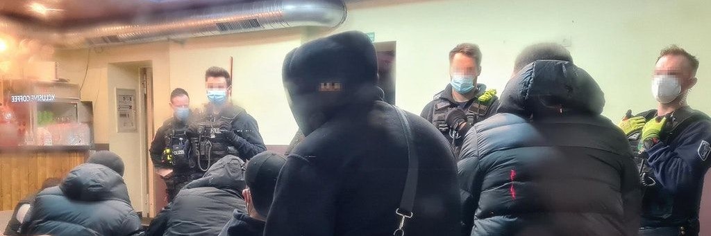 Polizisten mit Mundschutz stehen in der Bar und überprüfen die Anwesenden.