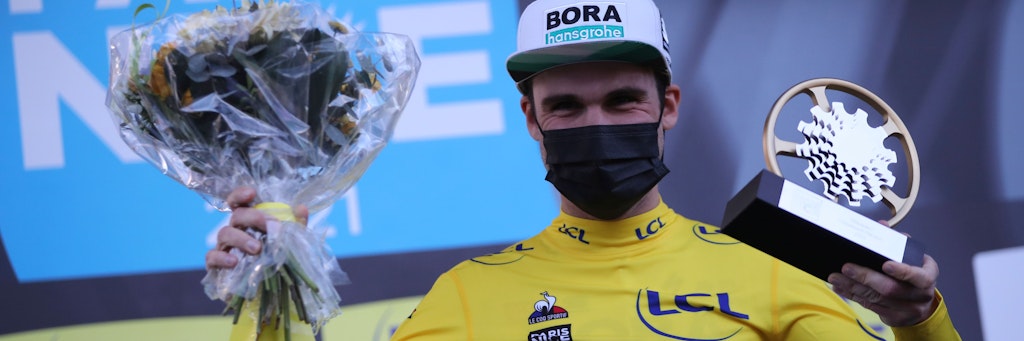 Maximilian Schachmann jubelt mit Blumenstrauß und dem Pokal.