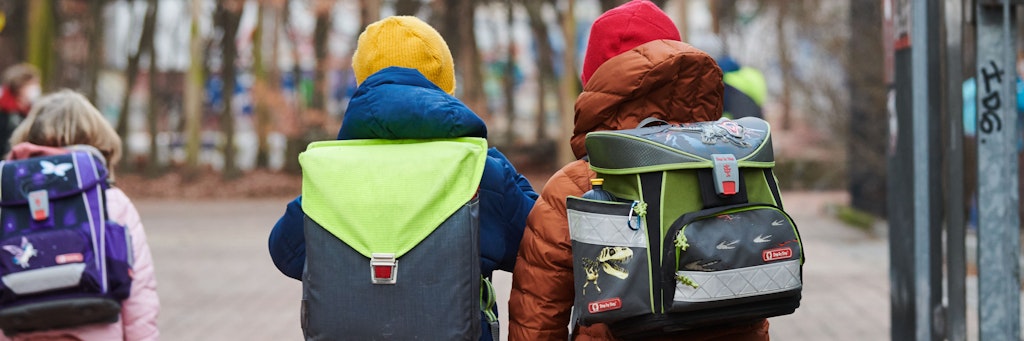 Drei Schüler gehen mit Schulranzen zum Eingang einer Grundschule.