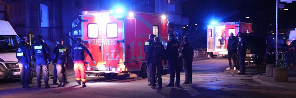 Rettungskräfte der Feuerwehr und Polizisten stehen an einer Kreuzung im Wrangelkiez. Die beiden schwer verletzten Opfer liegen in den Rettungswagen. 