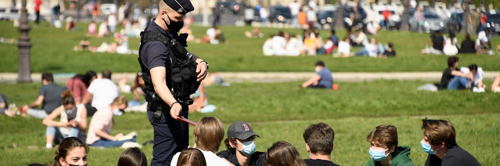 Ein Polizist kontrolliert bei sonnigem Frühlingswetter Menschen in einem Park in Paris. Ab dem Oster-Wochenende gelten in Frankreich wegen steigender Corona-Zahlen wieder Bewegungseinschränkungen. 