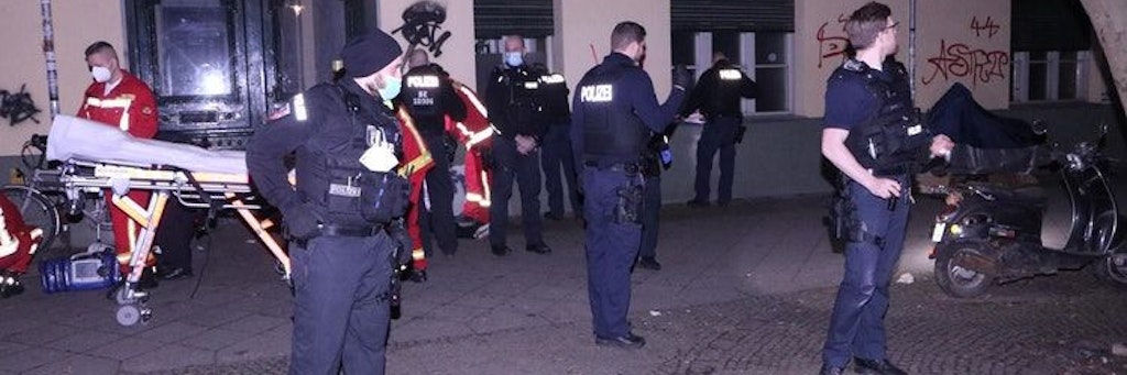 Polizisten stehen am Tatort an der Ratiborstraße, während Rettungskräfte den schwerverletzten 22-Jährigen behandeln