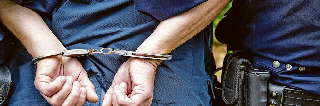Ein Polizist führt einen Mann in Handschellen ab (Symbolbild).