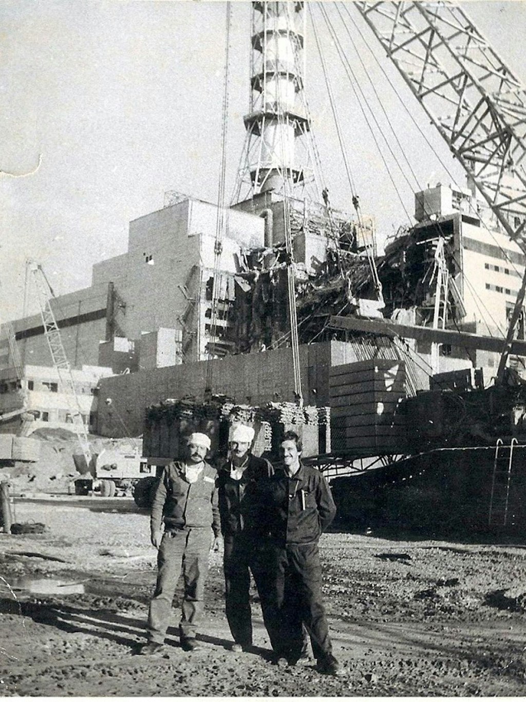 Die Aufnahme, die um den 25. August 1986 entstanden ist, zeigt die erste, gut 17 Meter hohe Kaskade des ersten Betonsarkophags am explodierten Block vier des Atomkraftwerks Tschernobyl. Davor steht Ilja Suslow (r.) mit zwei Kollegen für ein Erinnerungsfoto. 