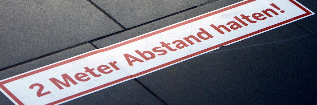 Eine Markierung mit der Aufschrift "zwei Meter Abstand halten" auf dem Boden.