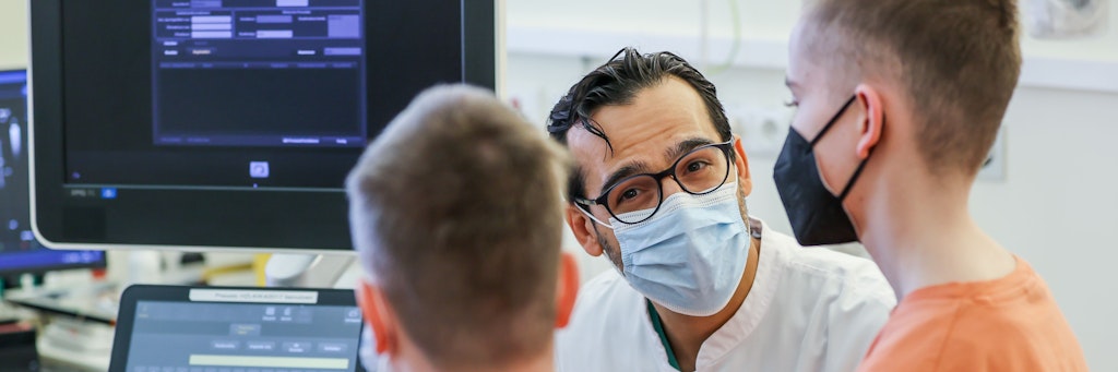Diyar Saeed, Leiter des Herztransplantationsprogramms, erklärt etwas während einer Nachsorgeuntersuchung der Zwillinge Jamie (im Vordergrund) und Kilian (r.) am Herzzentrum Leipzig.