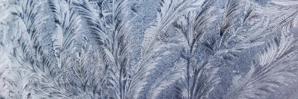 Eisblumen haben sich in einer frostigen Nacht auf der Frontscheibe eines Autos gebildet.