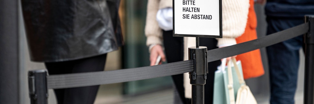 Neben einer Schlange vor einem Geschäft am Kudamm steht ein Hinweisschild mit der Aufschrift "Bitte halten Sie Abstand". 