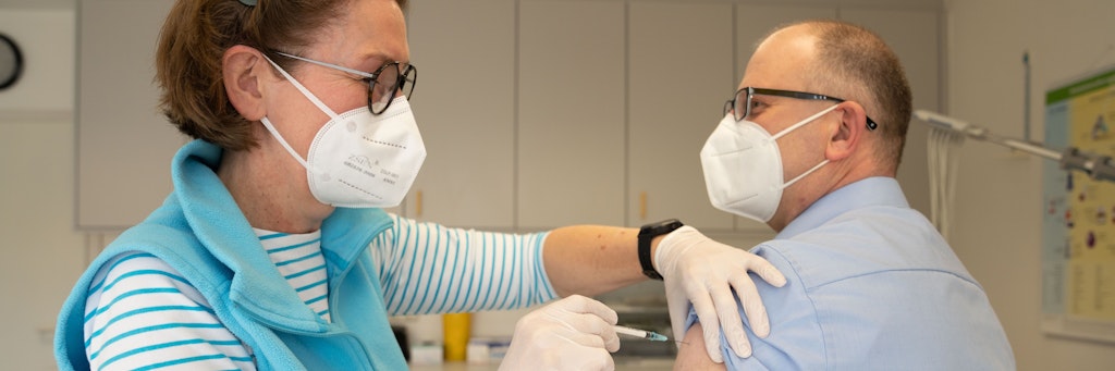 Eine Hausärztin impft in ihrer Praxis einen Patienten.