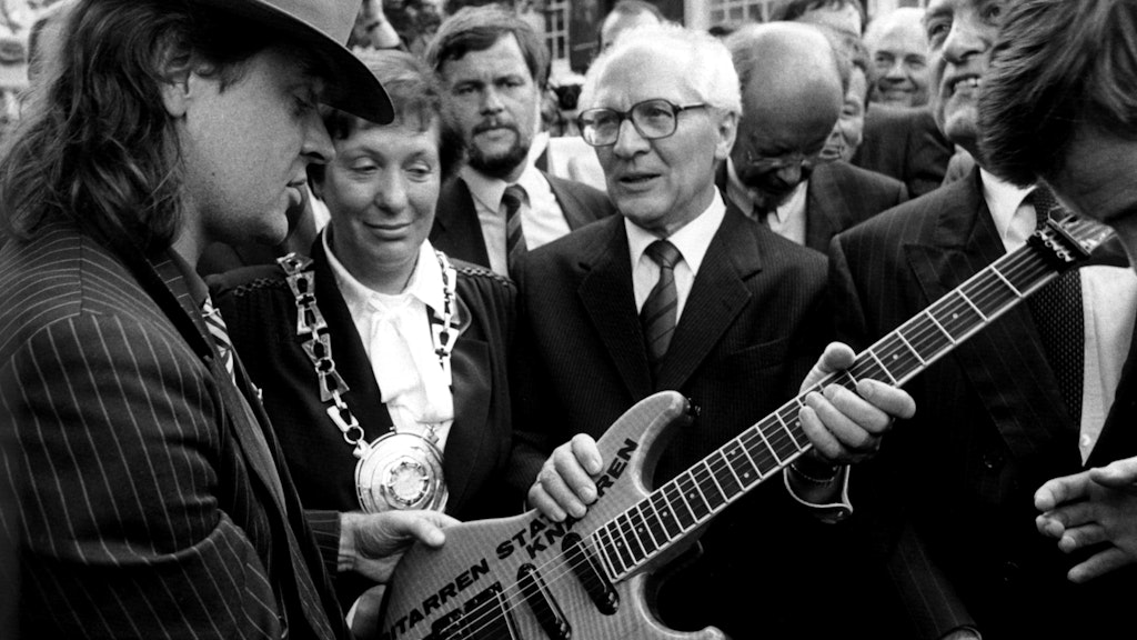 Rockmusiker Udo Lindenberg (l.) überreicht dem ehemaligen SED-Generalsekretär Erich Honecker (M.) eine Gitarre mit der Aufschrift „Gitarren statt Knarren“.