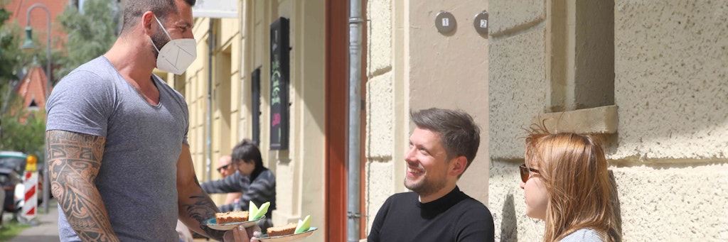 Der erste Tag: Seit Freitag darf die Gastronomie draußen wieder servieren. Oliver Koster, Chef von Die Kaffeefreunde, bringt frischen Kuchen für Heiko Franz (37) und Enikö Koklacs (35).