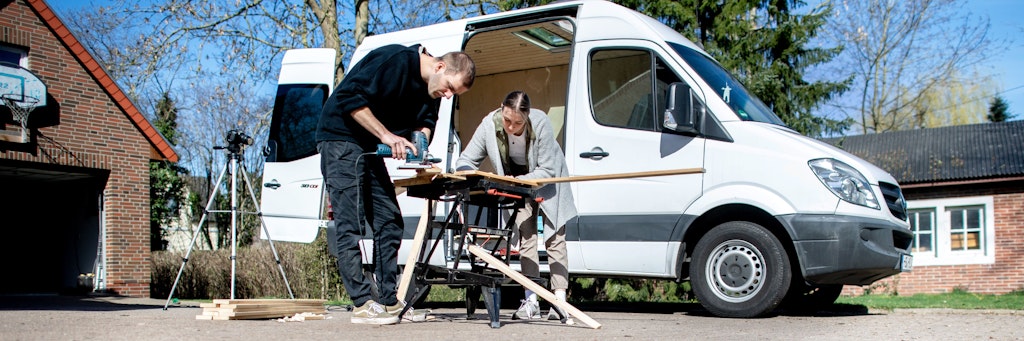 Greta Thomas und Hannes Wehrmann sägen Holz vor ihrem Mercedes-Benz Sprinter, den das Paar in Eigenarbeit zu einem Campervan umbaut. 