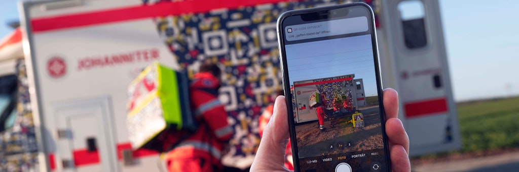 In einer gestellten Szene wird eine Unfallsituation mit einem Smartphone fotografiert. Das Handy erkennt den QR-Code.