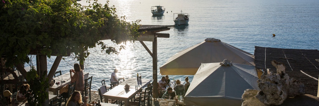 Touristen sitzen in einem Café am Meer in Limeni, einem kleinen Fischerhafen auf der Halbinsel Mani. 