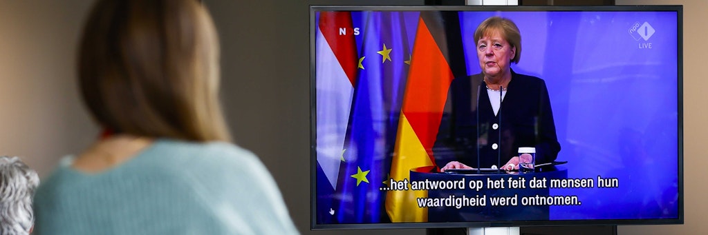 Eine Frau verfolgt die live übertragene Rede von Angela Merkel vor dem Fernsehapparat. 