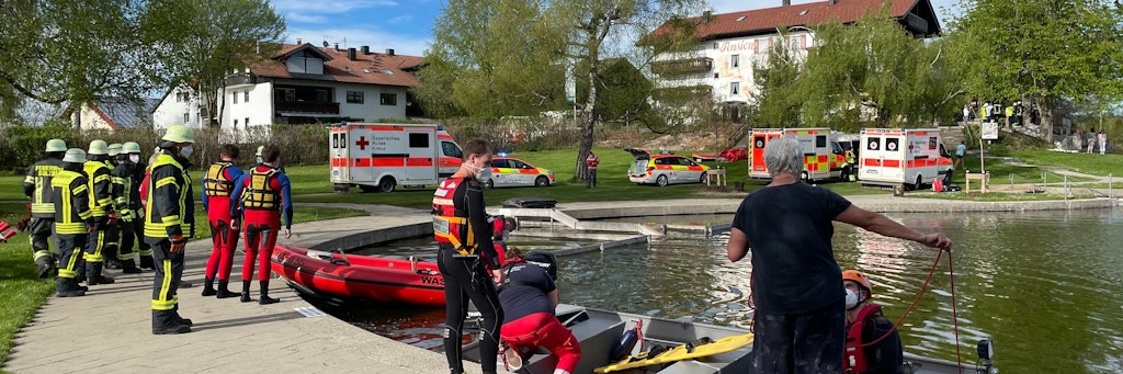 Einsatzkräfte der Feuerwehr und Rettungsdienste stehen an einem Badesee bei Sulzberg im Oberallgäu. Ein Kleinflugzeug mit vier Menschen an Bord ist kurz nach dem Start in den See gestürzt.