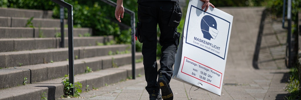 Ein Mann bringt ein abgehängtes Hinweisschild zur Maskenpflicht zu seinem Fahrzeug. Laut den vom Senat beschlossenen Lockerungen der Corona-Einschränkungen fällt die abstandsunabhängige Maskenpflicht in den Grünanlagen entlang von Alster und Elbe seit dem 22. Mai 2021 weg. 
