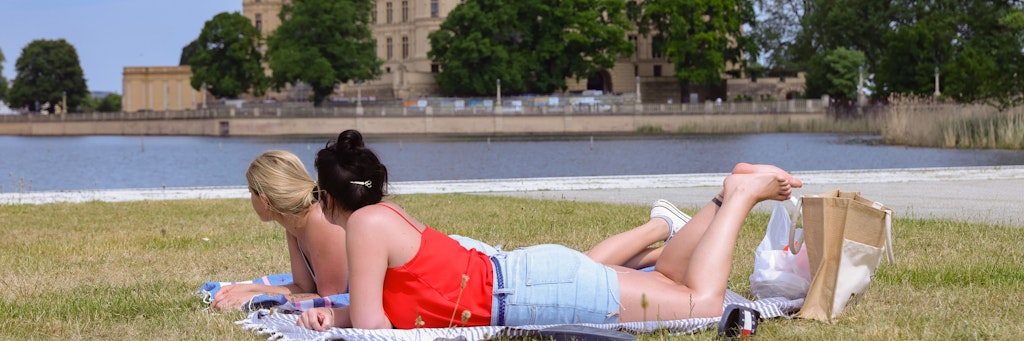 Zwei Frauen liegen bei sommerlichem Wetter auf einer Wiese vor dem Schweriner Schloss. Die Landeshauptstadt von Mecklenburg-Vorpommern hat eine Inzidenz von null - dort wurden also keine Corona-Neuinfektionen binnen sieben Tagen registriert.
