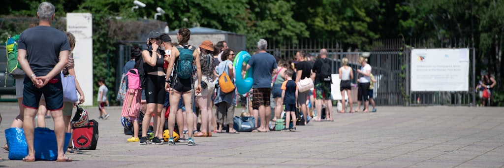 Menschen stehen bei warmem Wetter in einer Schlange vor dem Eingang zum Olympiabad.