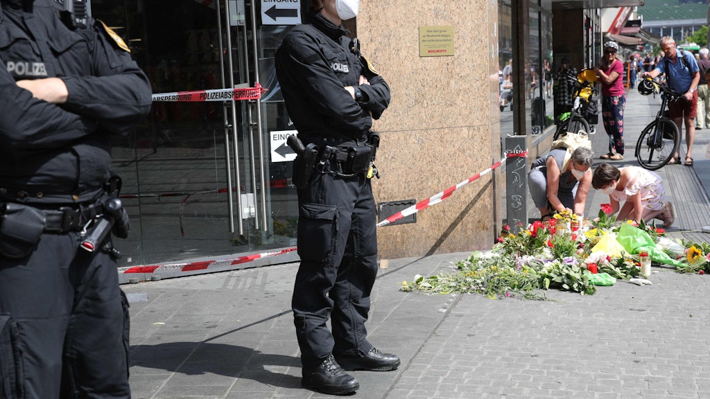 Passanten legen vor dem Tatort - eine Woolworth-Filiale in Würzburg - Blumen und Kerzen nieder.
