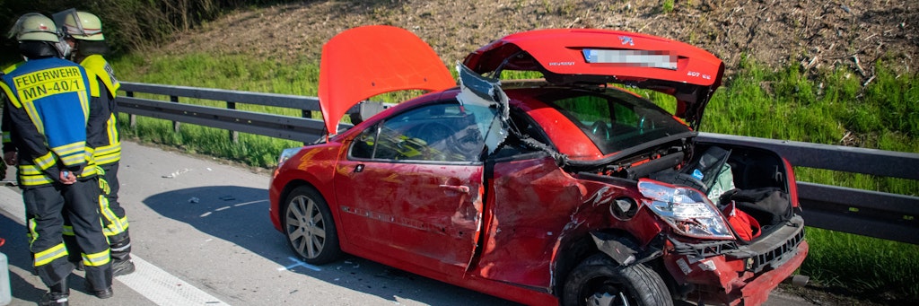 Einsatzkräfte der Feuerwehr stehen am Unfallort neben dem Autowrack. 