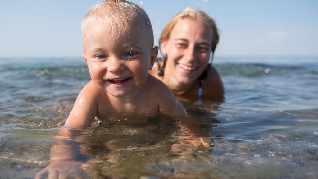 Eltern sollten schon früh dafür sorgen, dass ihre Kinder Spaß am Wasser haben. Dieser kleine Junge planscht vergnügt am Ufer. Seine Mama bleibt konsequent in Griffweite – so kann sie zupacken, falls etwas passiert. 