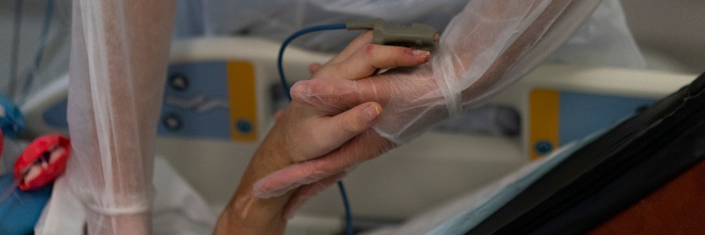 Eine Krankenschwester hält die Hand eines Coronavirus-Patienten an einem Beatmungsgerät.