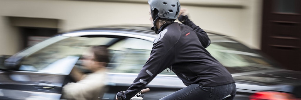 Immer wieder kommt es zu vermeidbaren Fahrradunfällen: Ein Autofahrer öffnet die Fahrertür, während sich eine Radfahrerin von hinten nähert.