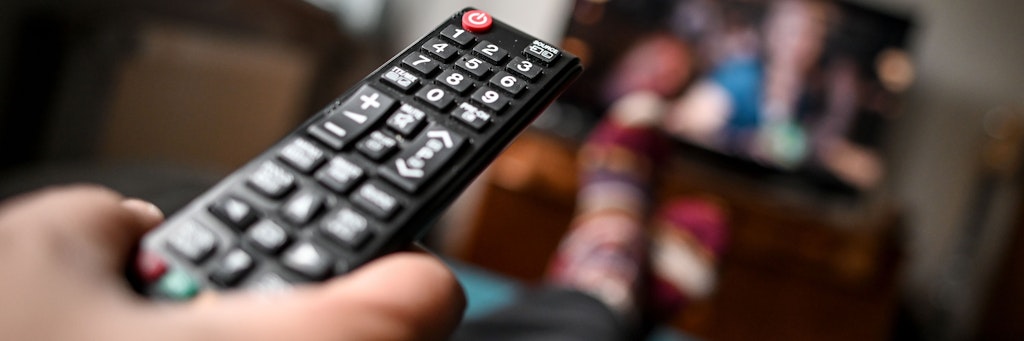 Ein junger Mann sitzt mit einer Fernbedienung vor dem Fernseher.