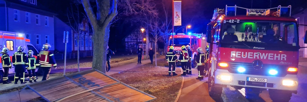 Feuerwehrleute stehen am Einsatzort in Beelitz, wo ein Spaziergänger von diesem Wahlplakat erschlagen wurde.
