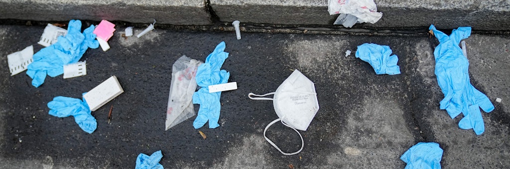 Einmalhandschuhe, FFP2-Maske und benutzte Corona-Antigen-Testkits liegen am Morgen auf der Straße vor einem Corona-Testzentrum.
