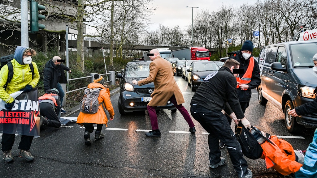 Der Mann im beigen Mantel schubste die Person in der orangenen Jacke um.