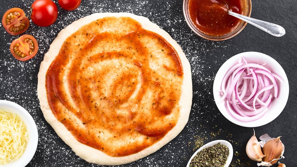 Der fertige Pizzateig wird ausgerollt und nach Herzenslust belegt - zum Beispiel mit Tomatensoße, Zwiebeln, Tomaten und Co.