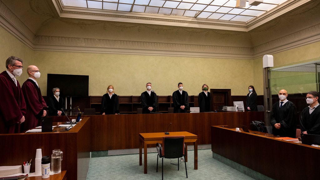 Die Beteiligten im Prozess wegen Vorbereitung einer schweren staatsgefährdenden Gewalttat und Terrorfinanzierung stehen zu Beginn der Verhandlungen im Gerichtssaal. Der Angeklagte ist nicht im Bild.