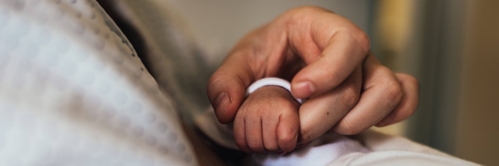 Ein Vater hält im Krankenhaus die Hand seines Babys (Symbolfoto).