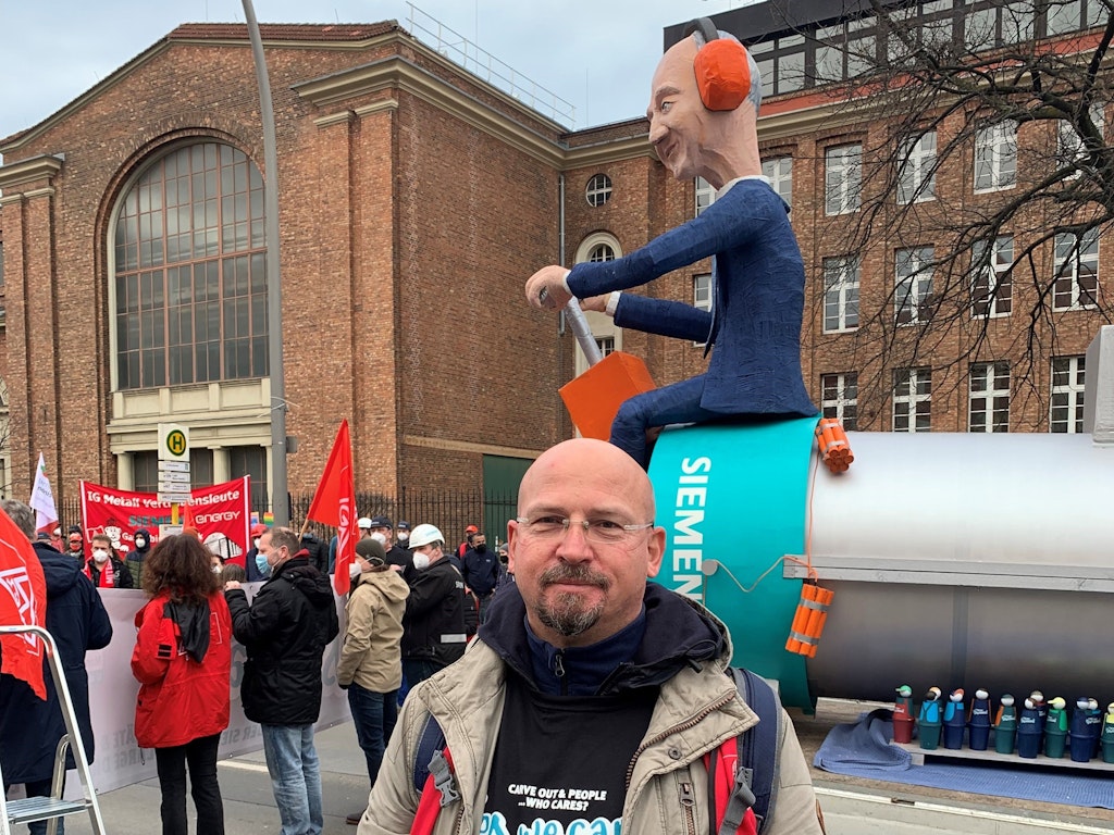 Matthias Reifenberger, Vertrauensmann der IG Metall im Dynamowerk. Hinter ihm die Puppe des Siemens-Chefs, der auf einem Elektromotor hockt und dabei ist, Motor, Mitarbeiter und sich in die Luft zu sprengen.