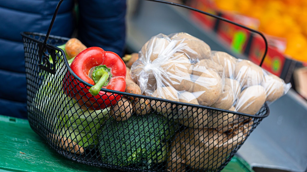 Der mit Paprika, Brokkoli, Kartoffeln und anderen Lebensmitteln gefüllte Korb einer Kundin steht auf einer Kiste an einem Stand auf einem Wochenmarkt. Gemüse ist in Deutschland zuletzt deutlich teurer geworden.