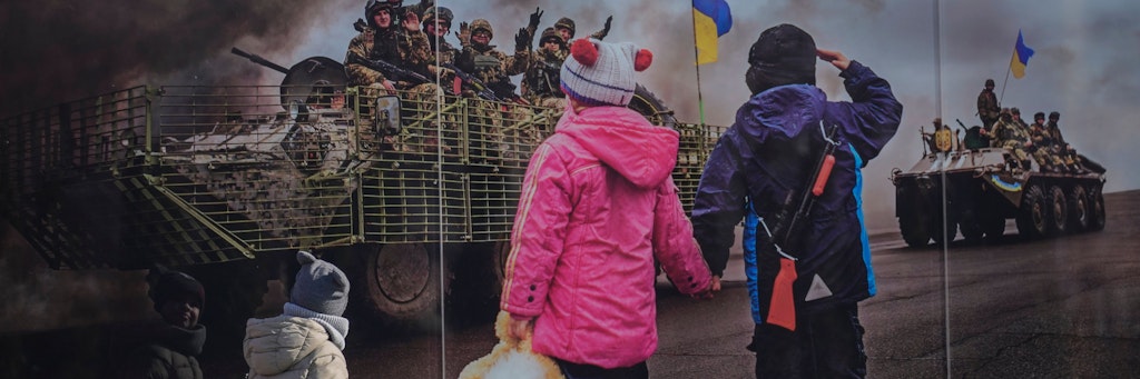Ukrainische Kinder gehen an einem großformatigen Bild, aufgestellt im Gedenken an die ukrainischen Toten der Konfrontation zwischen dem ukrainischen Militär und den prorussischen Separatisten, vorbei. Wie erklärt man Kindern in Deutschland den Krieg?