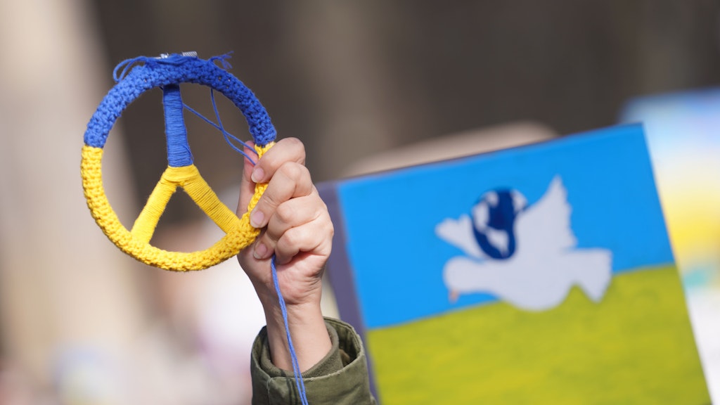 Ein Demoteilnehmer zeigt ein Friedenszeichen, bestrickt in den Farben der Ukraine.