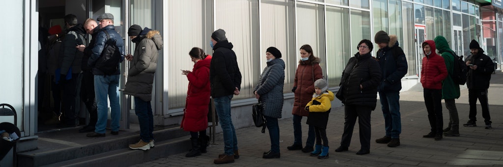 Menschen stehen in einer Schlange, um Geld von einem Geldautomaten der Alfa Bank abzuheben.