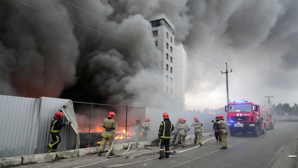 Einsatzkräfte der Feuerwehr stehen vor einem Logistikzentrum in Kiew, das nach Beschuss in Brand geraten ist.