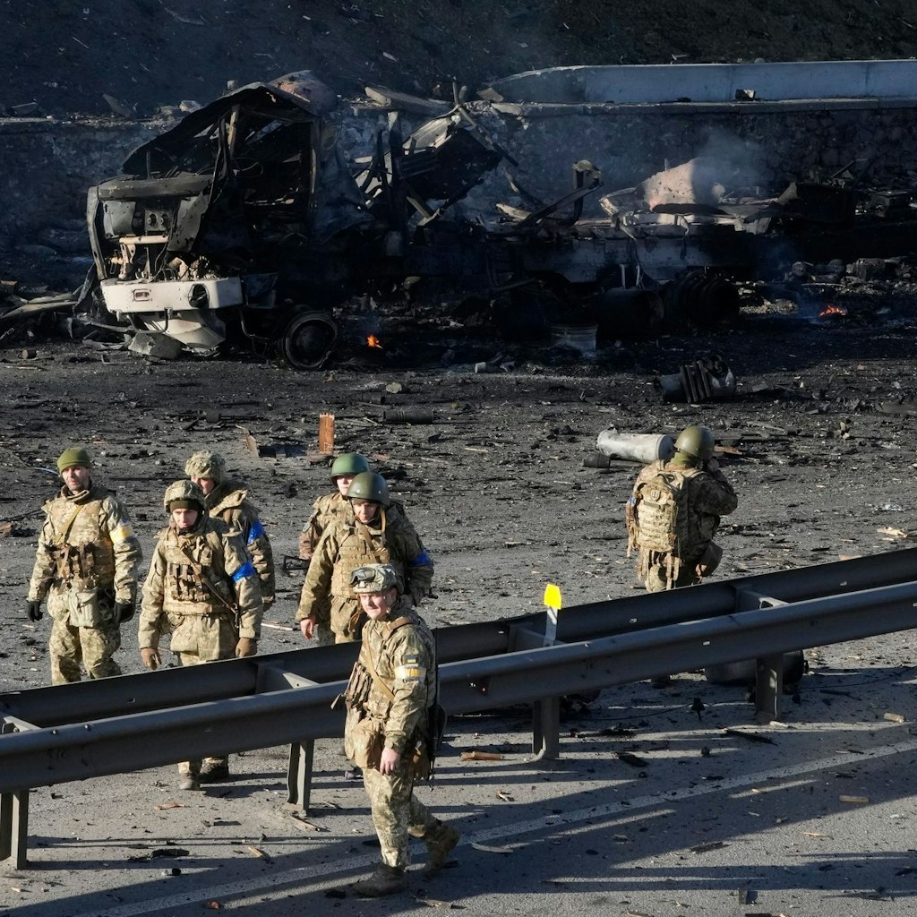 Ukrainische Soldaten in der Nähe von Trümmern eines brennenden Militärlastwagens auf einer Straße in Kiew.